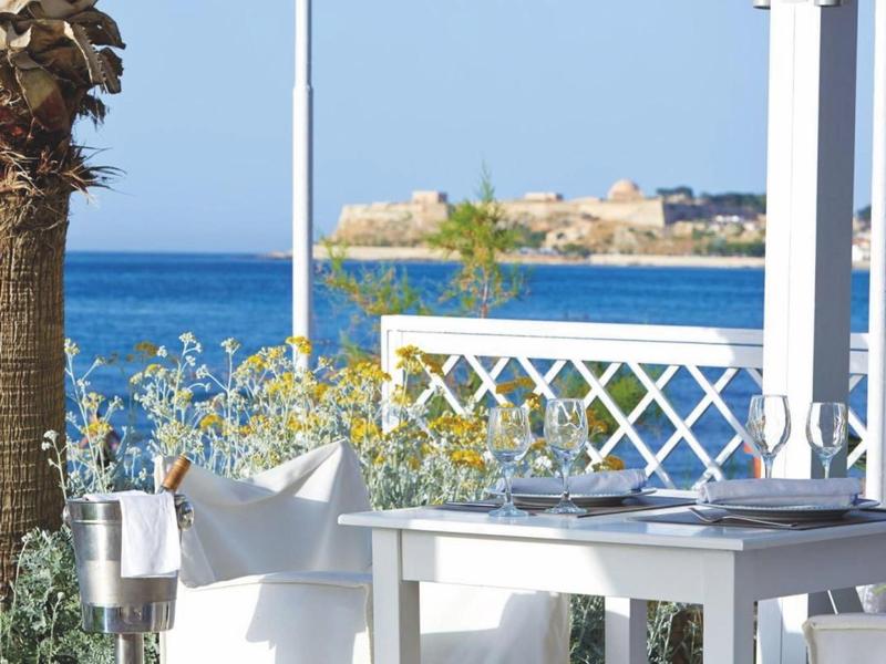 Biały nakryty stół na tarasie z widokiem na błękitne morze i nadmorskie miasto.
