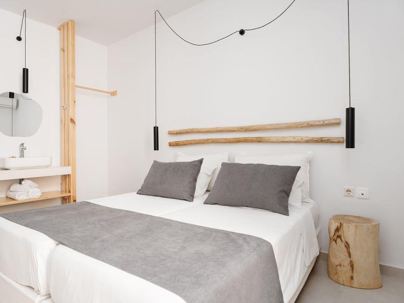 Jasno urządzone sypialnia z podwójnym łóżkiem, szarymi poduszkami i minimalistycznym wystrojem.