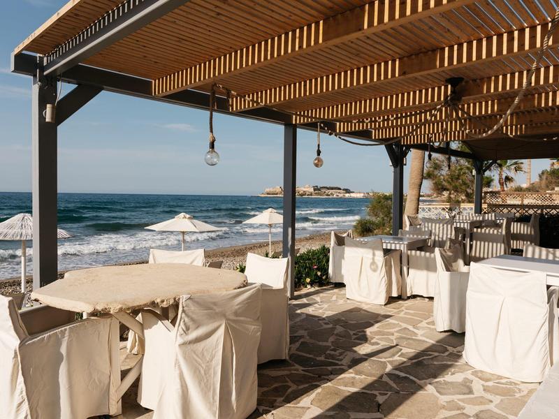 Zakryta część restauracji na plaży z stolikami i widokiem na morze.