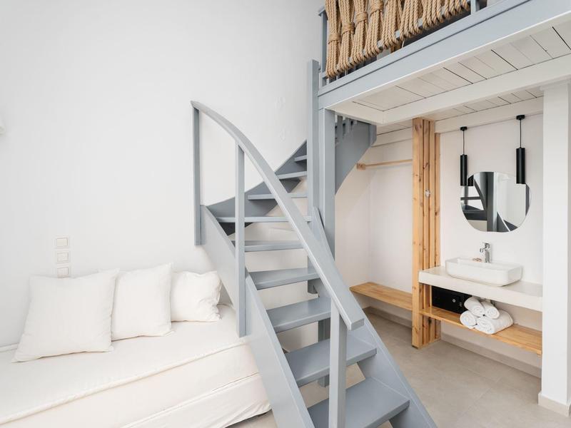 Jasny pokój z nowoczesną szarą spiralną klatką schodową, leżanką i drewnianymi detalami na lustrze i półce.