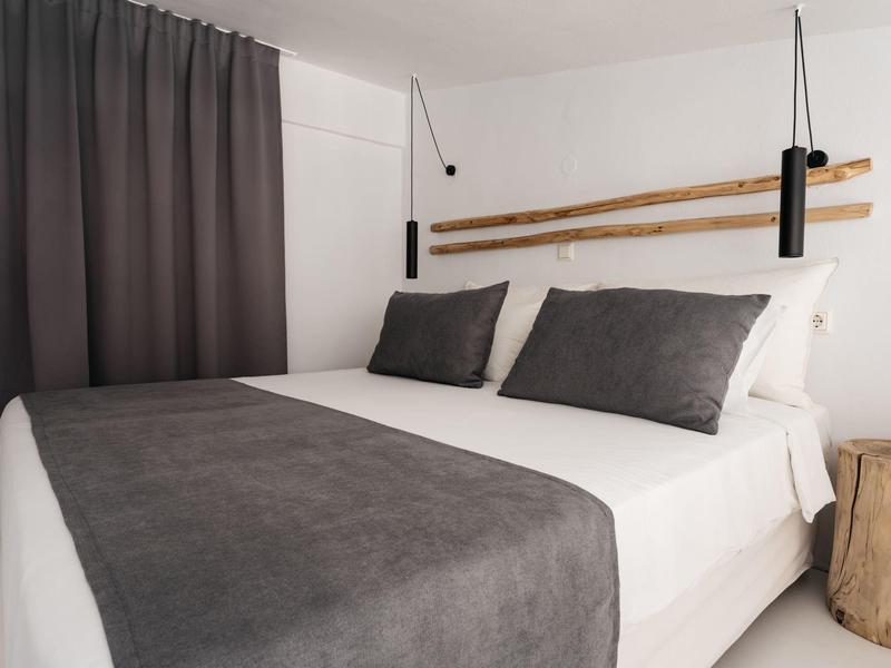 Nowoczesna sypialnia z białym łóżkiem, szarym kocem i zasłonami oraz minimalistycznym oświetleniem.