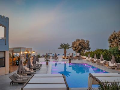 Nowoczesny basen hotelowy z leżakami i widokiem na morze o zachodzie słońca.