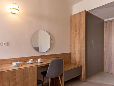 Nowoczesny pokój hotelowy z drewnianym biurkiem, okrągłym lustrem i szarym krzesłem.