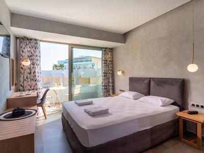 Nowoczesny pokój hotelowy z podwójnym łóżkiem, balkonem, biurkiem, telewizorem i neutralnym wystrojem.