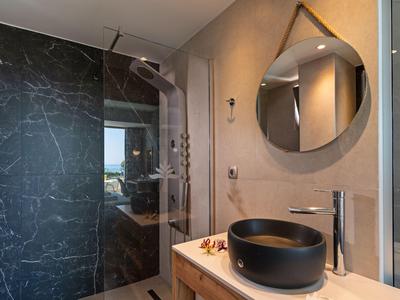 Nowoczesna łazienka z czarną kamienną umywalką, dużym lustrem i marmurową ścianą prysznicową.