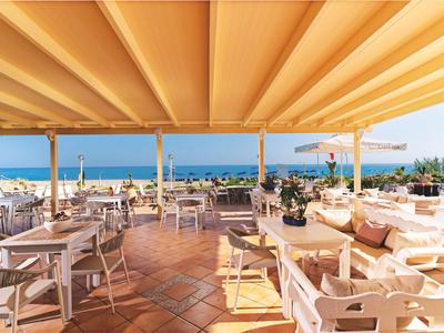 Otwarta część tarasu hotelowego z białymi krzesłami, stolikami i widokiem na morze w słoneczny dzień