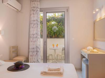 Jasny pokój hotelowy z łóżkiem podwójnym, stołem, krzesłami i balkonem z widokiem na zielone rośliny.