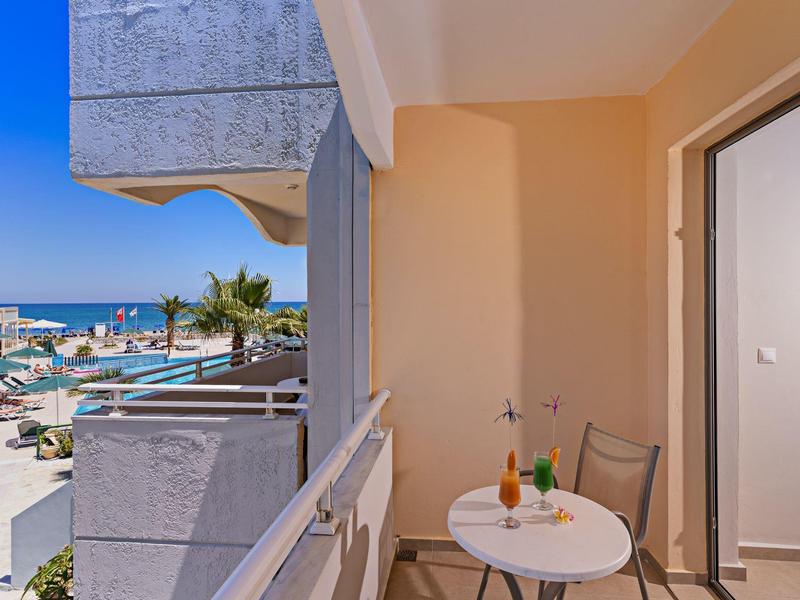 Balkon z małym stolikiem i dwoma krzesłami z widokiem na morze i plażę w tle.