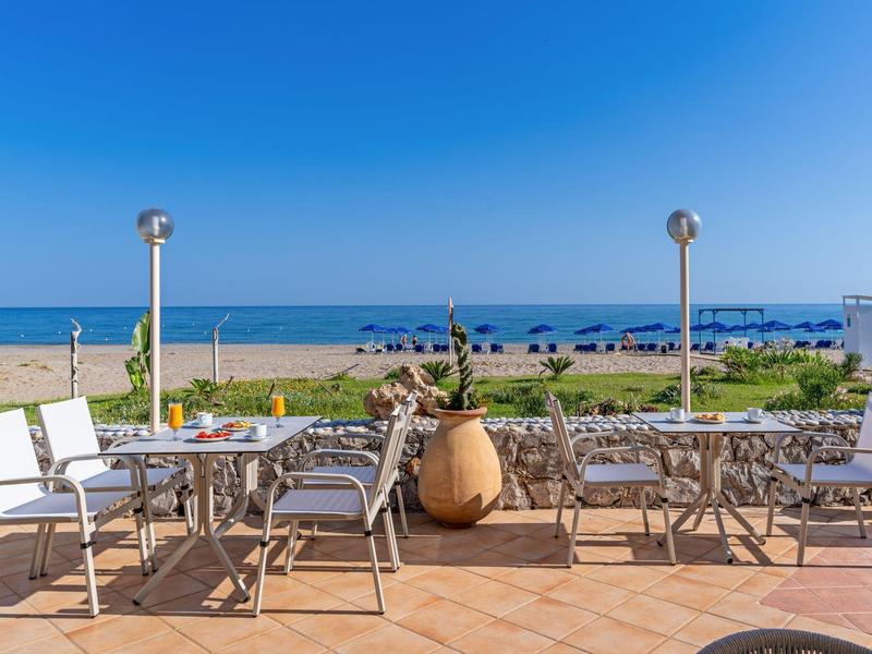 Pusta zewnętrzna przestrzeń z białymi krzesłami z widokiem na piaszczystą plażę i błękitne morze pod czystym niebem.