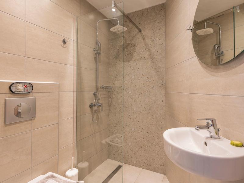 Mała nowoczesna łazienka hotelowa z prysznicem, umywalką i okrągłym lustrem.