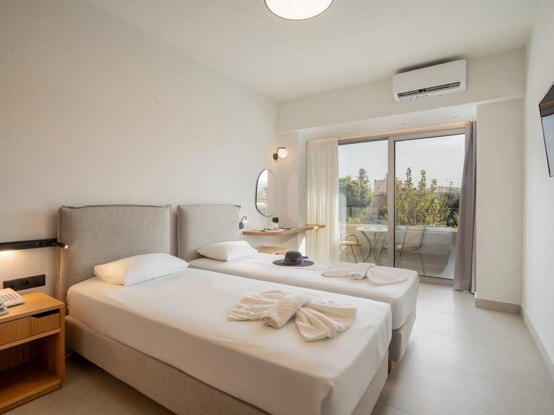 Jasny pokój hotelowy z dwoma pojedynczymi łóżkami, balkonem i nowoczesnym wyposażeniem.