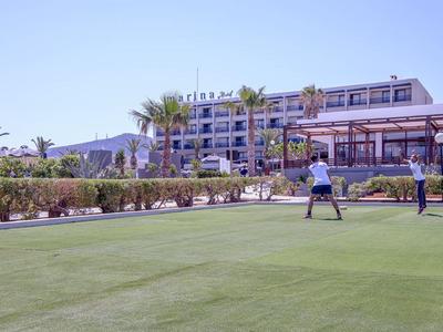 Persone che giocano a golf su un prato ben curato davanti a un hotel con palme e cielo limpido.