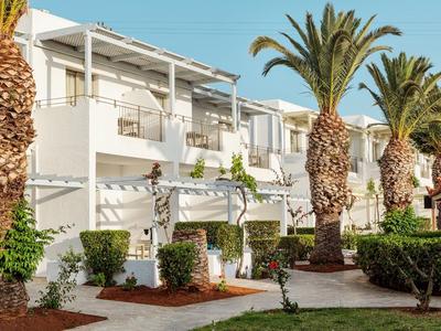 Case vacanze bianche con balconi e palme in un giardino curato sotto un cielo limpido.