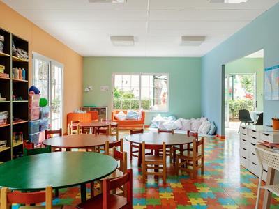 Barevná herna s stolem, židlemi, regály a výhledem do dvora.