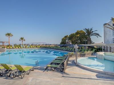 Area piscina dell'hotel con lettini, vasca idromassaggio e palme sotto un cielo limpido.