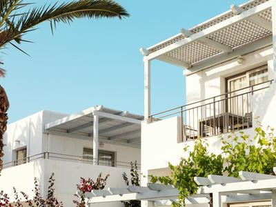 Complesso di edifici bianchi moderni con terrazza, piante e cielo azzurro sullo sfondo.