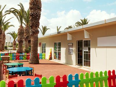 Venkovní prostor hotelu s barevným plotem, stoly a palmami za slunečného počasí