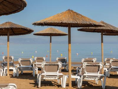 Prázdná lehátka a slámové slunečníky na písečné pláži s klidným mořem v pozadí.