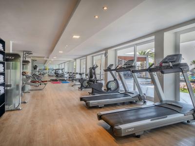 Palestra moderna con tapis roulant e attrezzi da ginnastica in una stanza luminosa e spaziosa con grandi finestre.