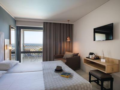 Moderně zařízený hotelový pokoj s manželskou postelí, posezením a balkonem s výhledem na moře.