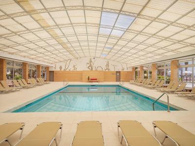 Krytý bazén s lehátky pod světlou, vzorovanou skleněnou střechou.