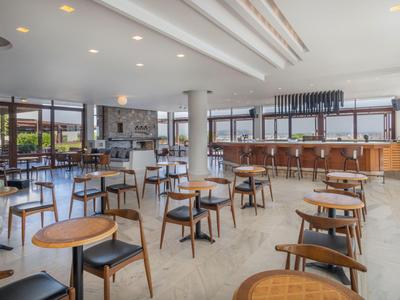 Bistrò moderno e luminoso con sedie e tavoli in legno, grandi finestre e un bancone bar.