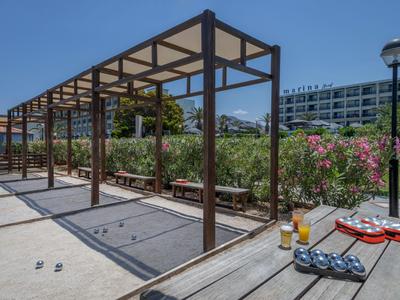Area esterna moderna con pergolato, panchine e un tavolo con bevande e piatti sotto un cielo azzurro.