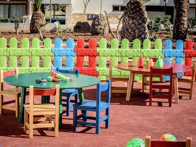 Barevné dětské stoly a židle na hřišti s jasným plotem.