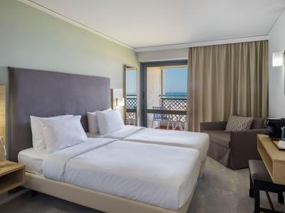 Moderní hotelový pokoj se dvěma lůžky, balkonem s výhledem na moře a útulným posezením.