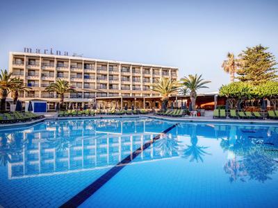 Hotel moderno con grande piscina all'aperto e palme sotto un cielo azzurro.