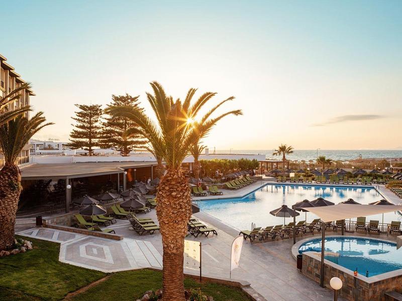 Hotelová bazénová oblast s palmami a lehátky při západu slunce