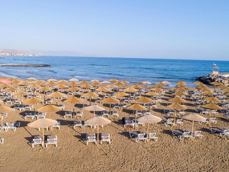 Pláž s mnoha slunečníky a lehátky u moře za slunečného dne
