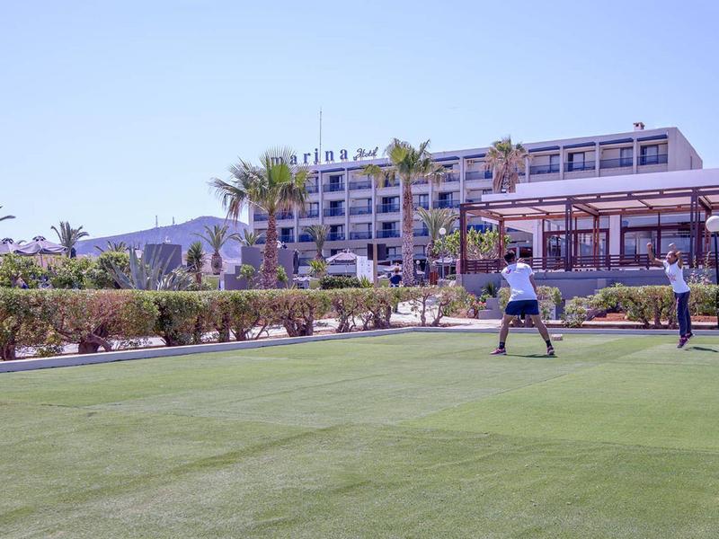 Dva lidé hrají golf na upravené zelené trávě před hotelem s palmami.