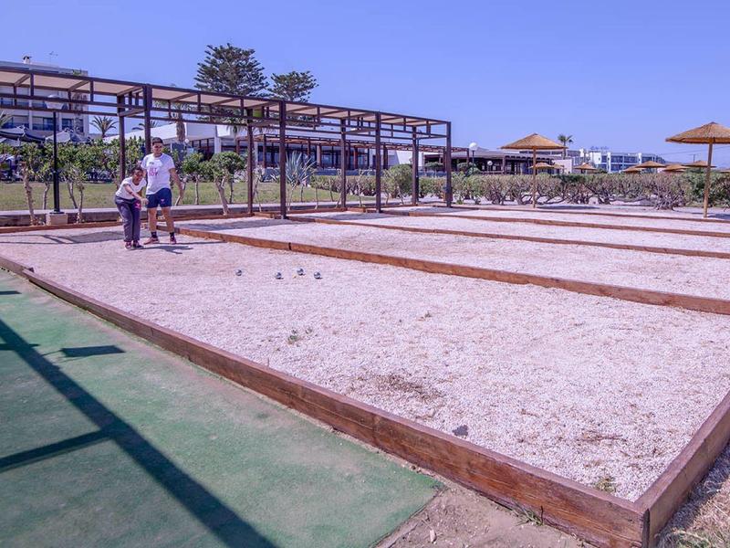 Několik hřišť na pétanque s pískem a dřevěnými rámy vedle hotelu a lehátek.