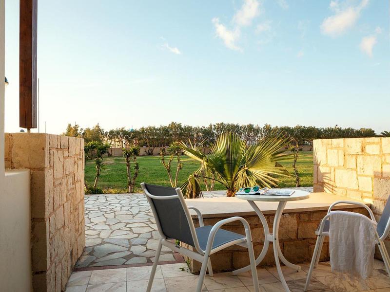 Terasa s bílým stolem a dvěma židlemi s výhledem na zelenou krajinu pod jasnou oblohou.