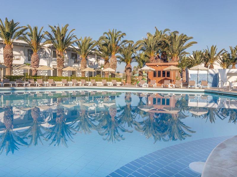 Velký bazén s palmami a bílými budovami v pozadí za slunečného dne.