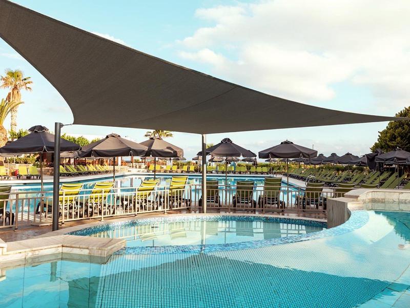 Bazénová zóna hotelového resortu s plachtou na stínění a lehátky