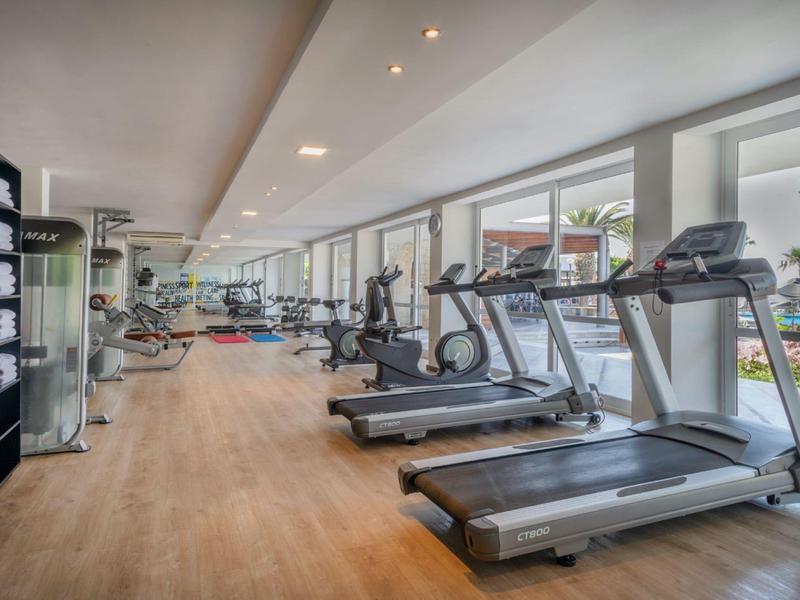 Moderní světlá posilovna s různými tréninkovými zařízeními a velkými okny s výhledem na terasu.