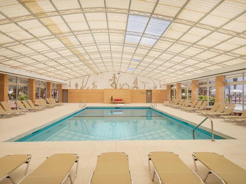 Krytý bazén s lehátky pod světlou, vzorovanou skleněnou střechou.