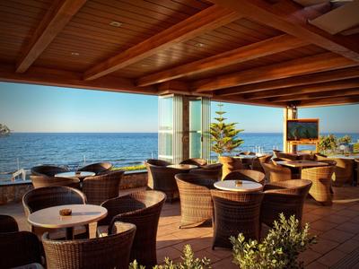 Terrazza coperta con poltrone in rattan di fronte al mare sotto un tetto di legno.