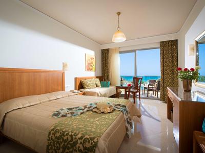 Camera d'hotel luminosa con letto grande, poltrona e balcone con vista sul mare.