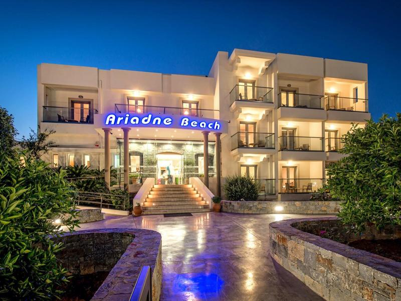 Hotel moderno illuminato di notte con balconi e ingresso circondato da piante.