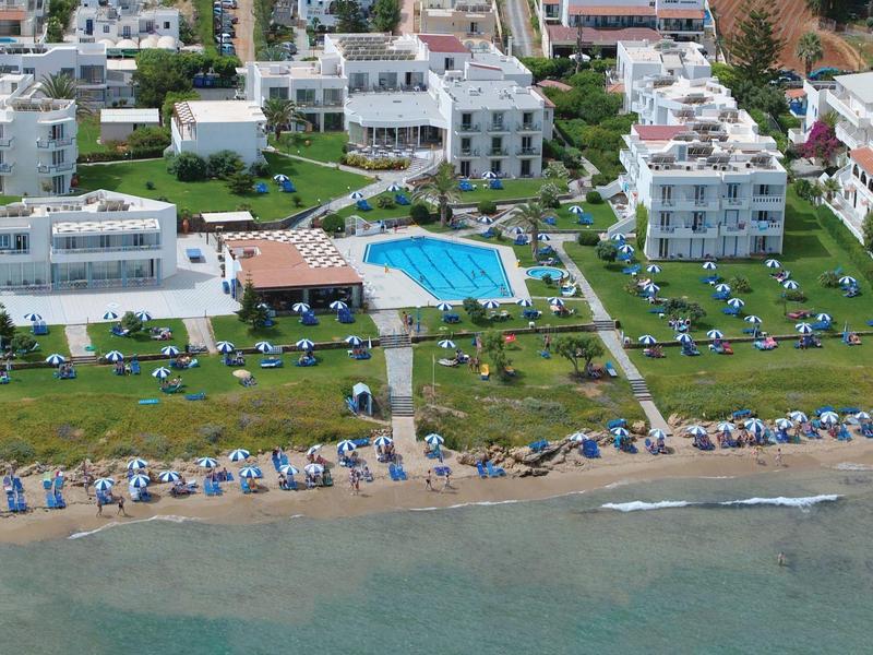 Veduta aerea di un hotel con piscina, lettini sull'erba e una spiaggia con ombrelloni.