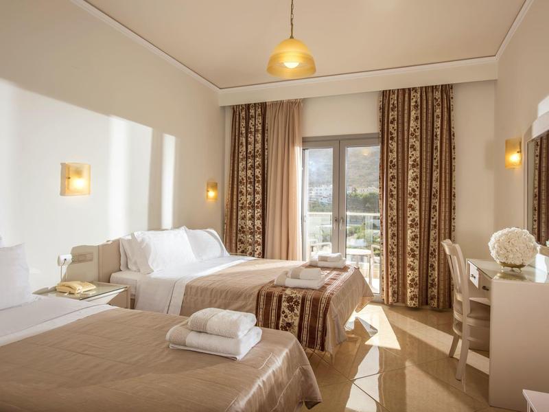 Camera d'albergo luminosa con due letti, mobili bianchi e grande finestra con vista sulla città.