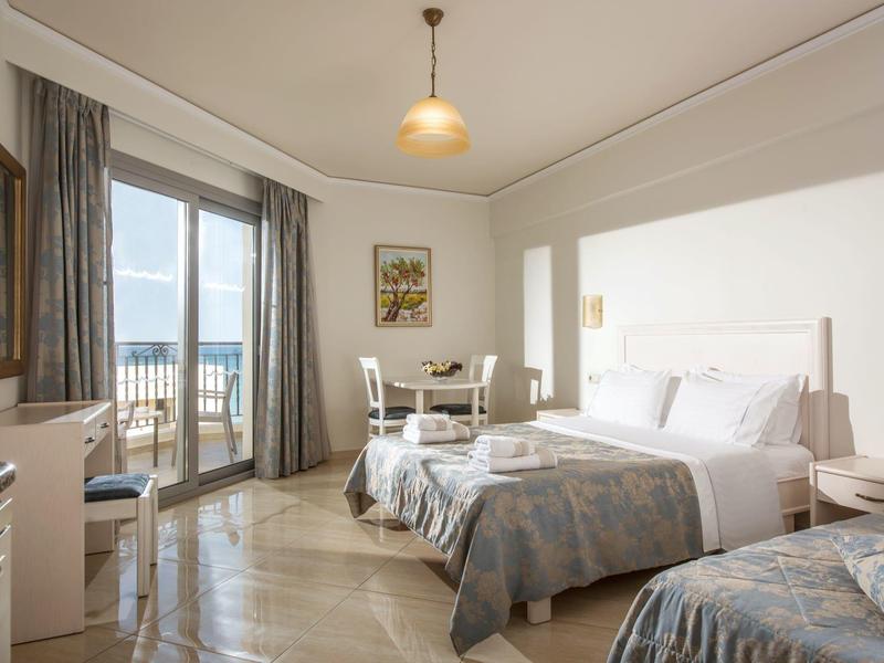 Camera d'hotel luminosa con due letti, balcone e vista sul mare.