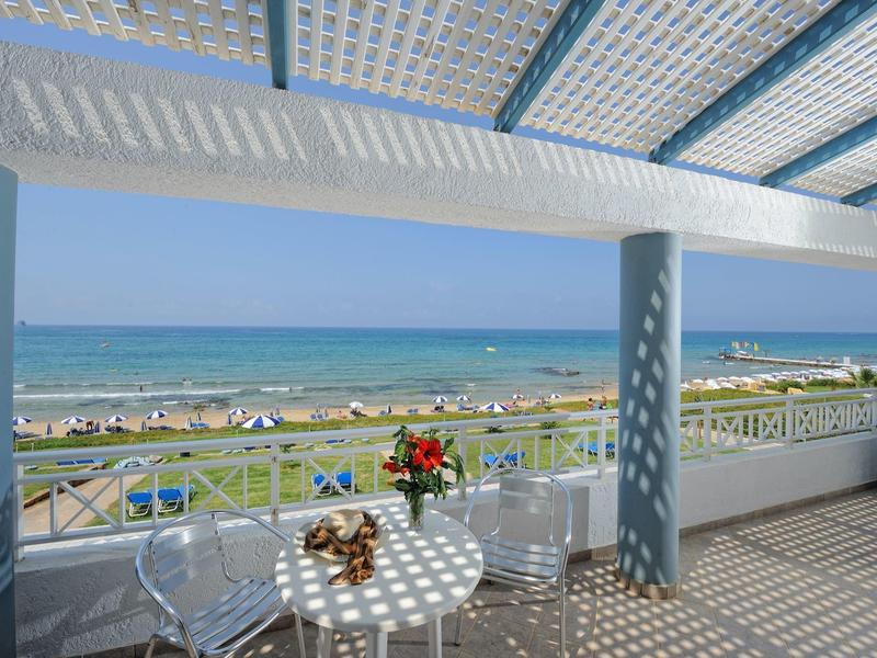 Vista da una terrazza con tavolo, sedie trasparenti, fiori, vista sul mare e sulla spiaggia.