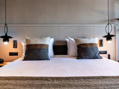 Nowoczesny pokój hotelowy z dużym łóżkiem, miękkimi poduszkami i wiszącymi lampkami nocnymi.