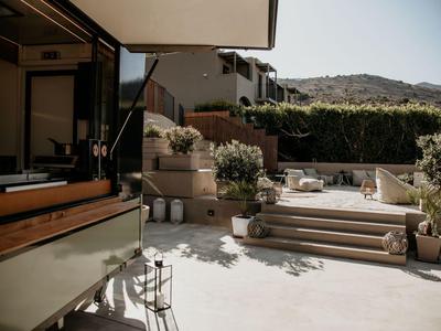 Słoneczne patio na zewnątrz z schodami, roślinami i nowoczesnym umeblowaniem pod zadaszeniem.