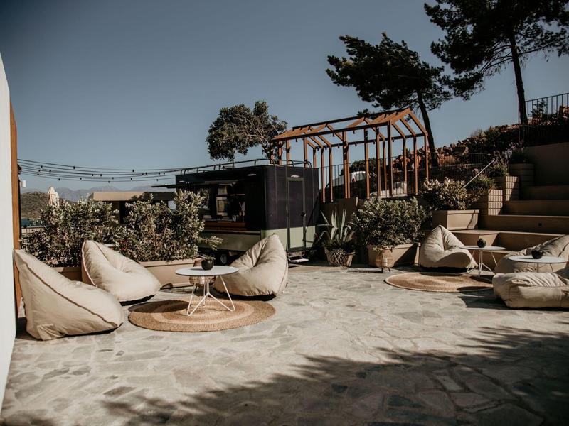 Przestrzeń na zewnątrz z pufami i drewnianymi stolikami pod konstrukcją przy schodach do ogrodu.