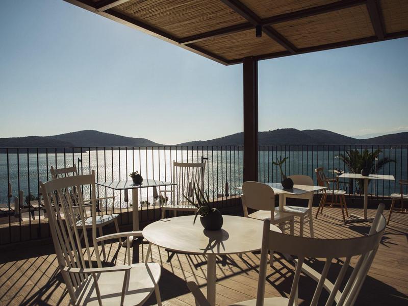 Taras na zewnątrz z stołami i krzesłami z widokiem na spokojne morze i odległe wzgórza.